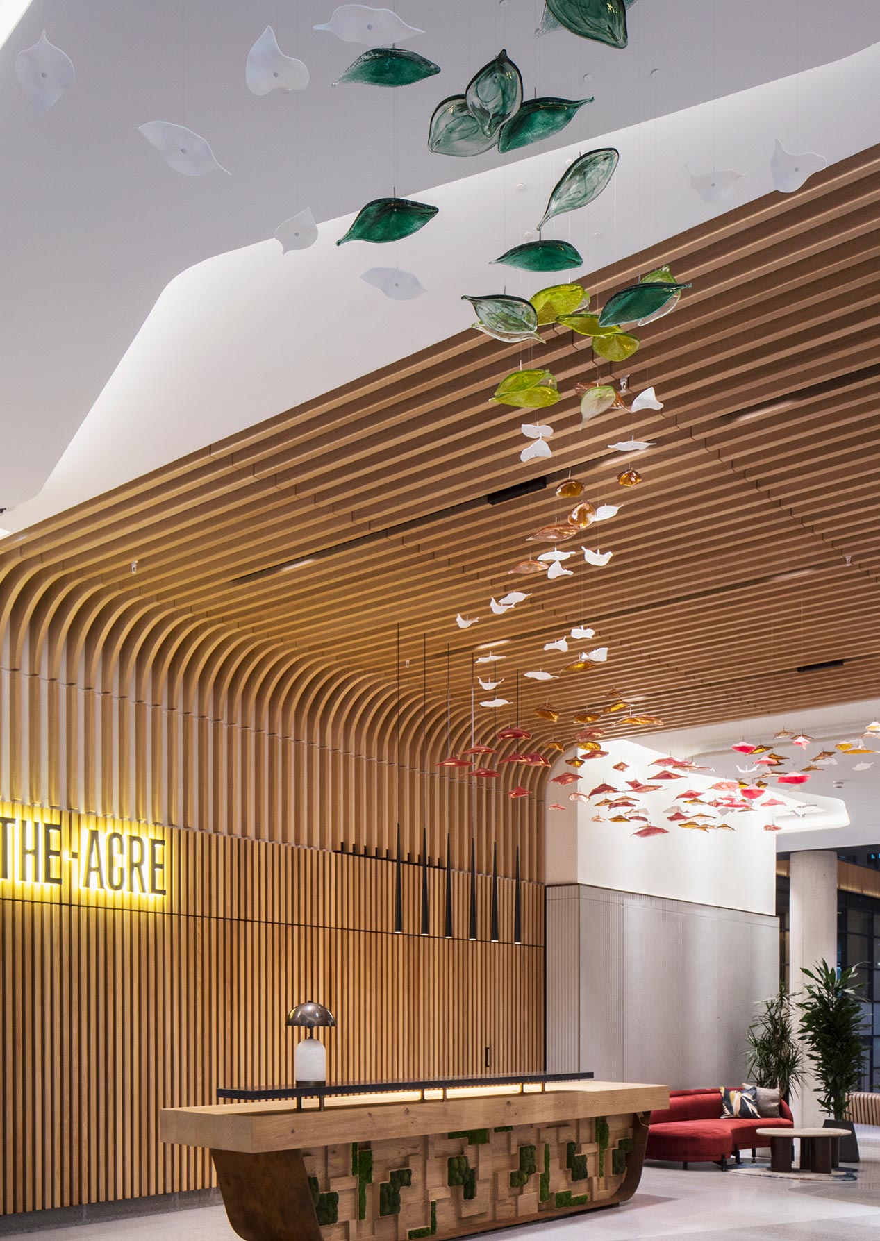 Colourful sweeping custom lighting installation made of glass and ceramic leaves in double-height lobby, by Nulty Bespoke